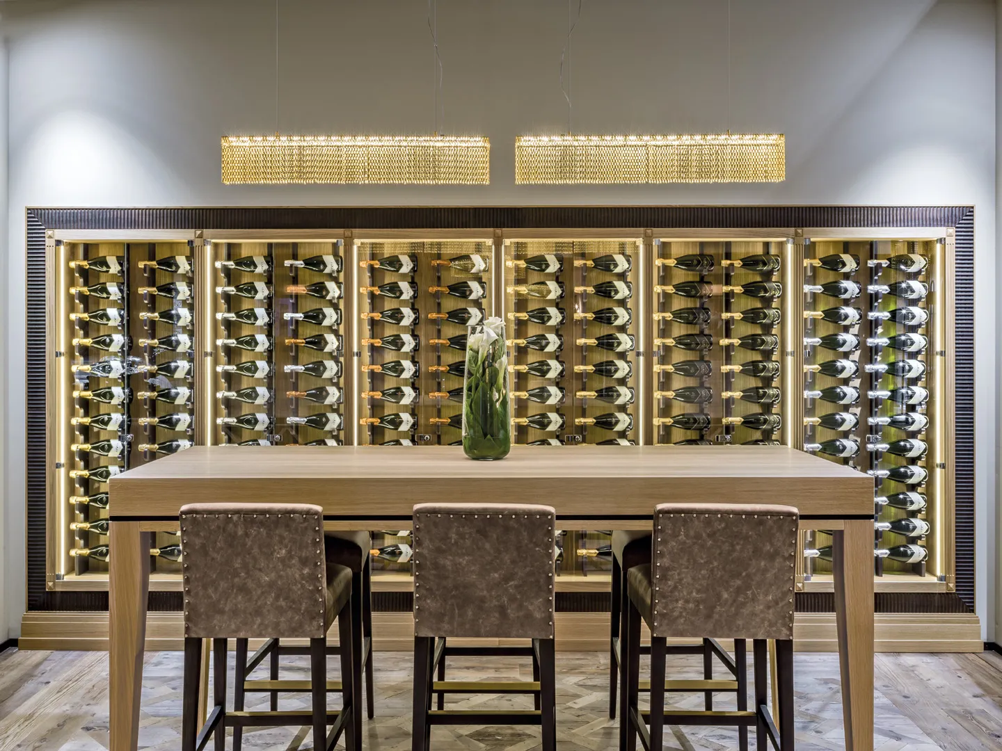 Zona vini Vendange Bernazzoli con pareti cantinetta illuminate e tavolo alto con sgabelli