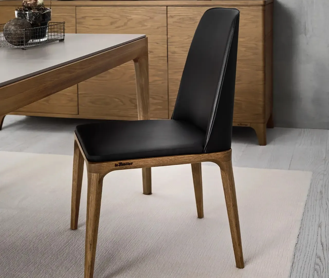 Sedia Chakra Le Fablier rivestita in nero con gambe in rovere accanto a un tavolo