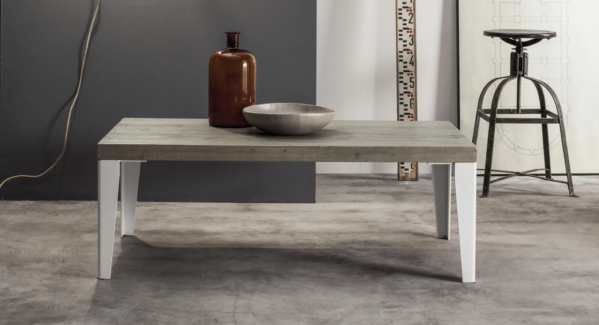 Tavolino Wood Devina Nais con piano grigio e gambe bianche accanto a uno sgabello