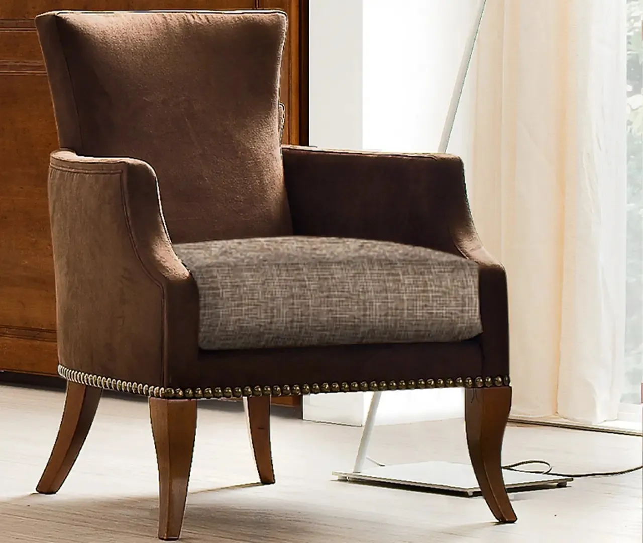 Poltroncina Apollo Le Fablier rivestita in tessuto marrone con borchie, accanto a una finestra