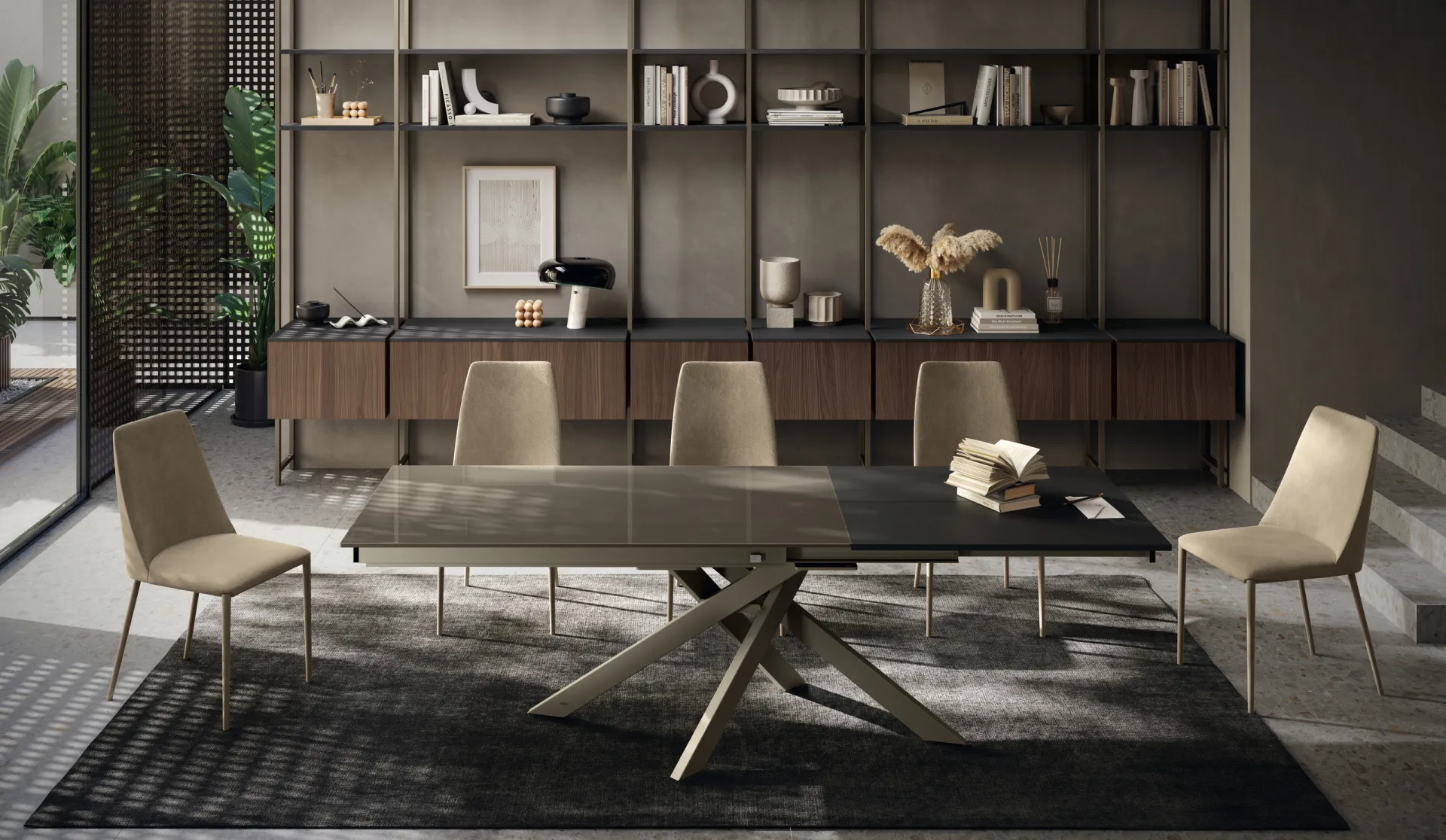 Tavolo Manhattan Scavolini con piano scuro e gambe incrociate chiare davanti a una libreria