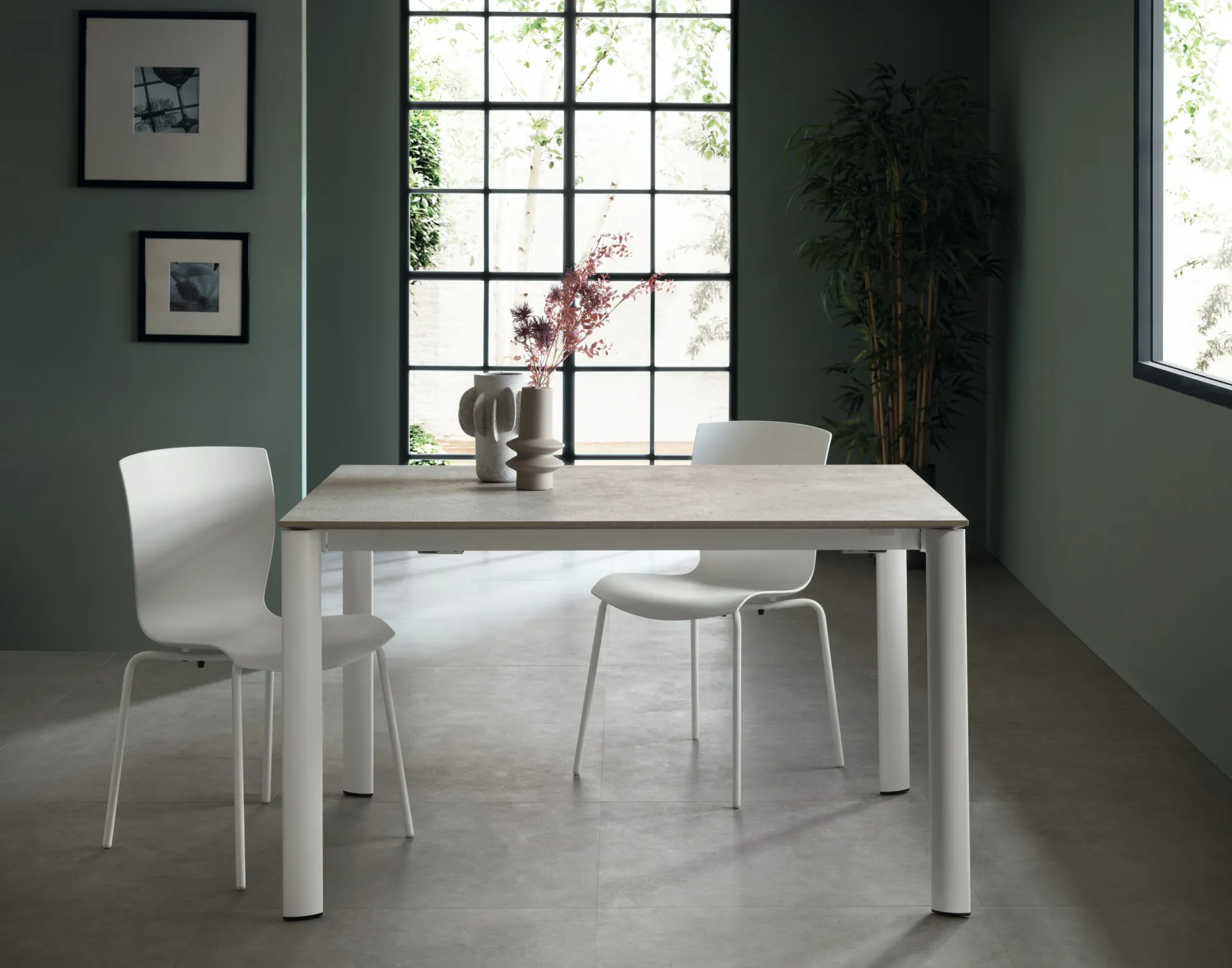 Tavolo Aiko Scavolini bianco con piano grigio chiaro e sedie bianche davanti a una parete verde