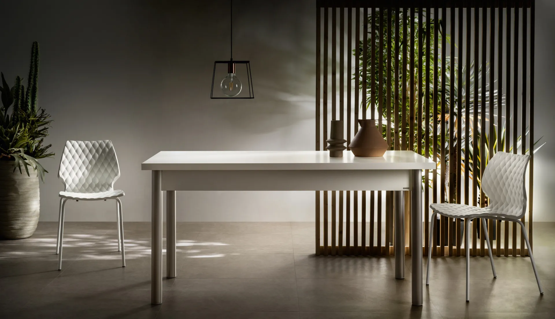 Tavolo Alis Scavolini bianco con gambe grigie e sedie trasparenti davanti a una parete a listelli