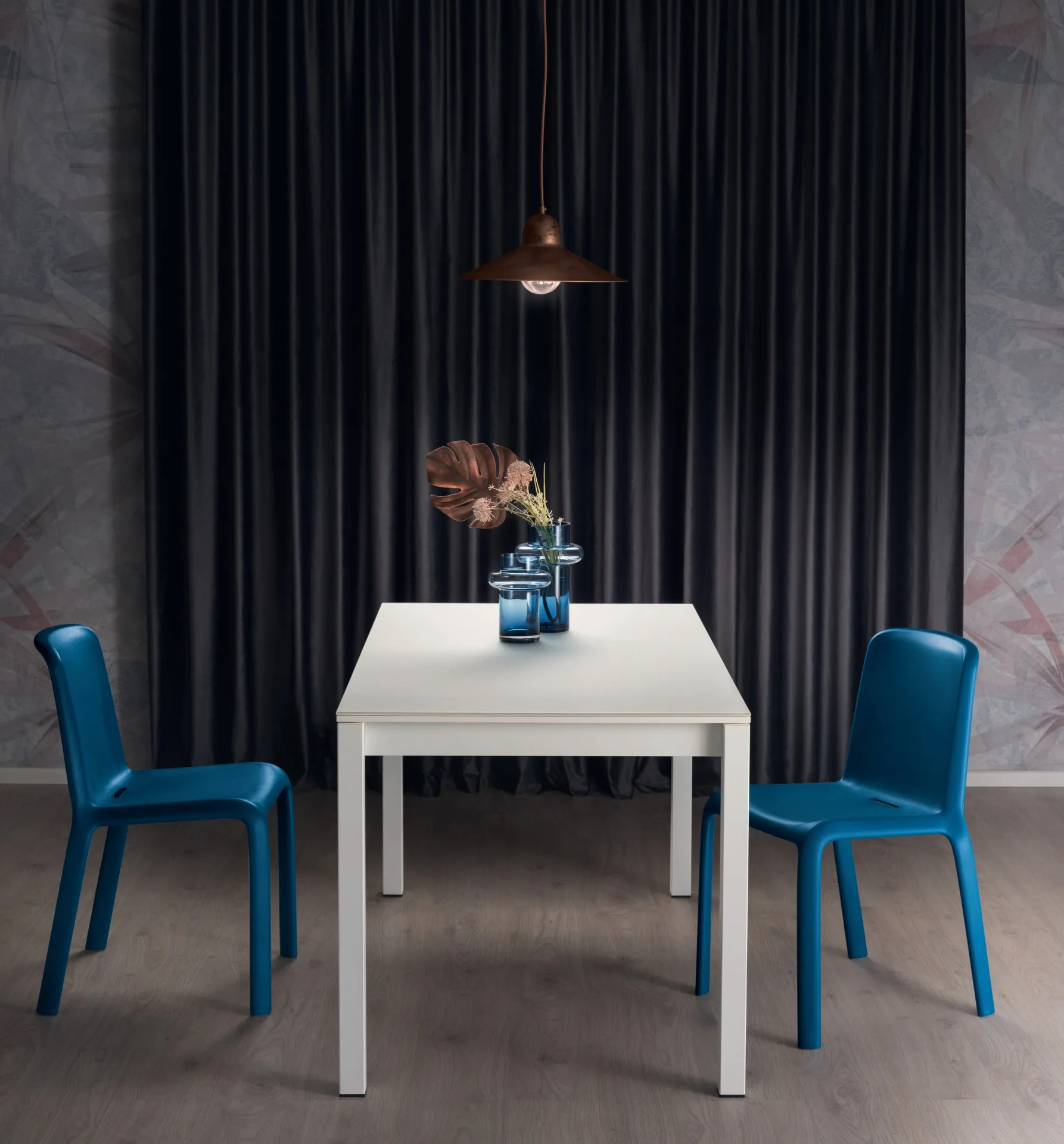 Tavolo Aliseo Scavolini bianco compatto con due sedie blu davanti a una tenda scura