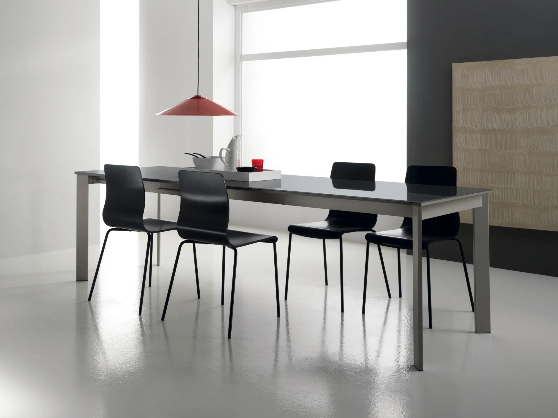 Tavolo Desko Scavolini aperto con piano scuro e sedie nere sotto una lampada rossa