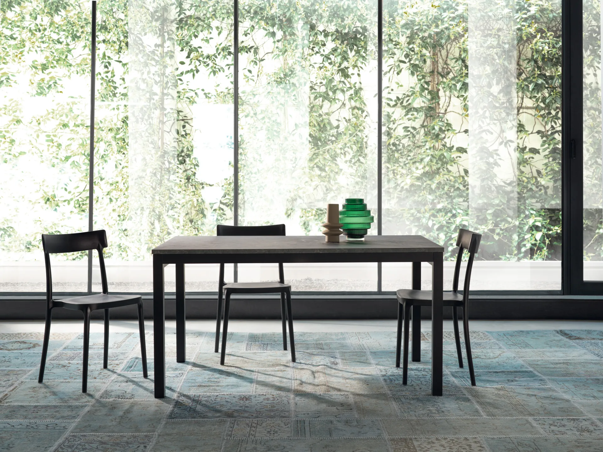 Tavolo Gulliver Scavolini grigio scuro con sedie nere davanti a una grande vetrata sul verde