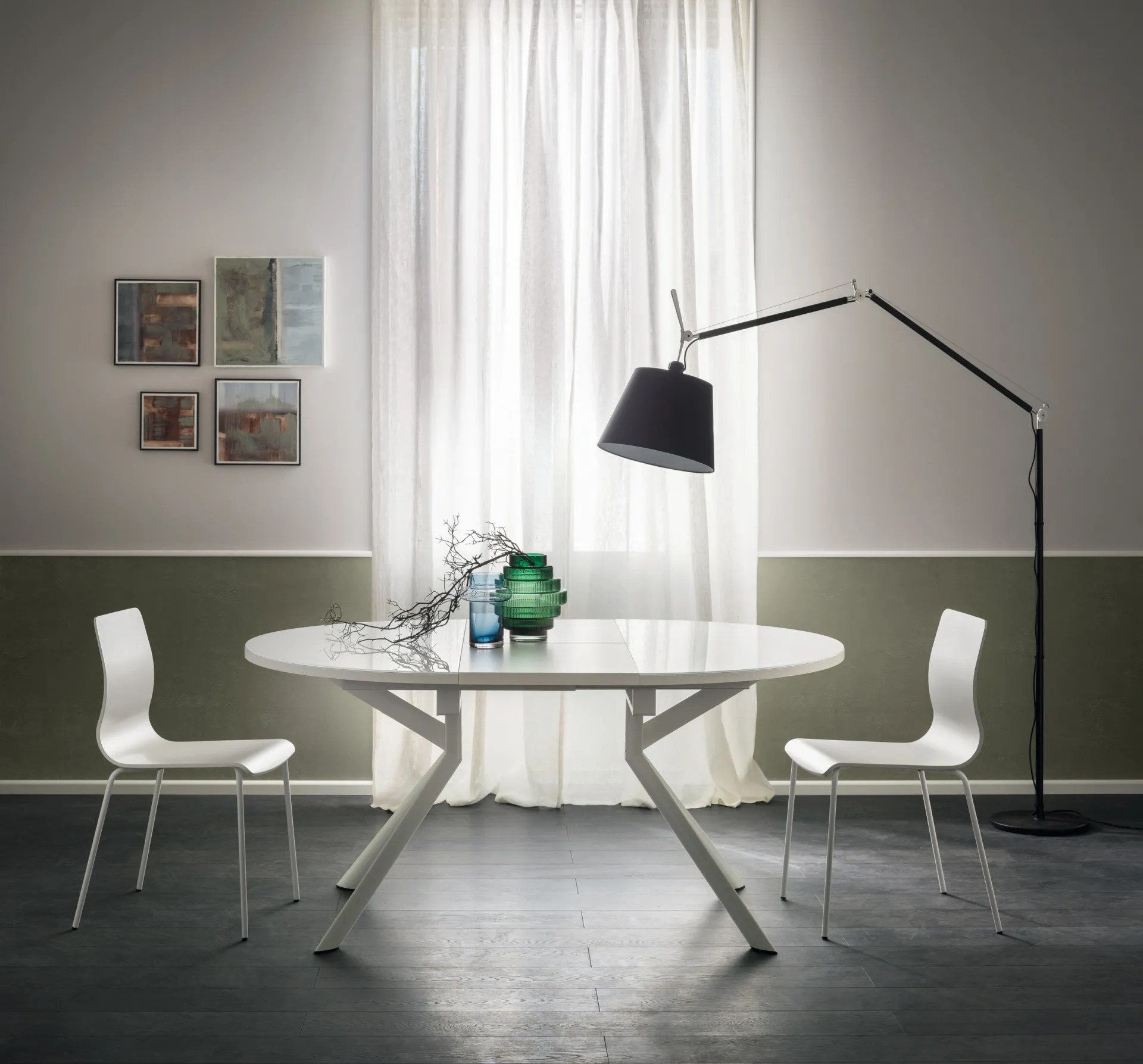 Tavolo Hover Scavolini bianco aperto in forma ovale, con gambe incrociate e due sedie bianche