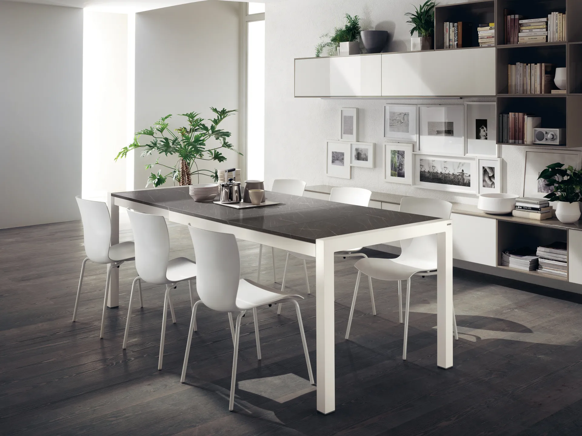 Tavolo Quadrifoglio Scavolini con struttura bianca, piano grigio scuro e sedie bianche davanti a una libreria