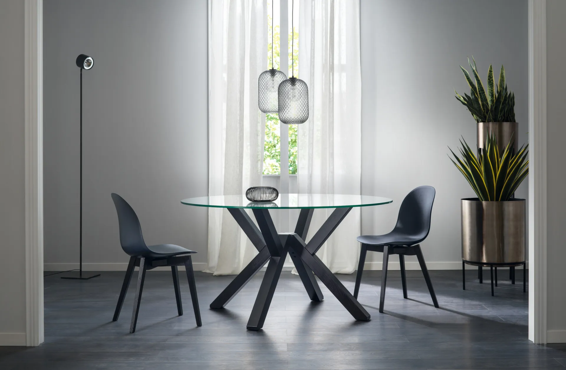 Tavolo Shangai Scavolini rotondo in vetro con base scura a gambe intrecciate e sedie nere