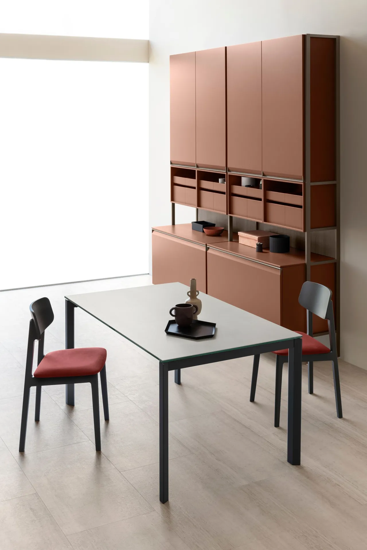 Tavolo Flawless Scavolini con piano chiaro e due sedie accanto a una parete attrezzata color terracotta
