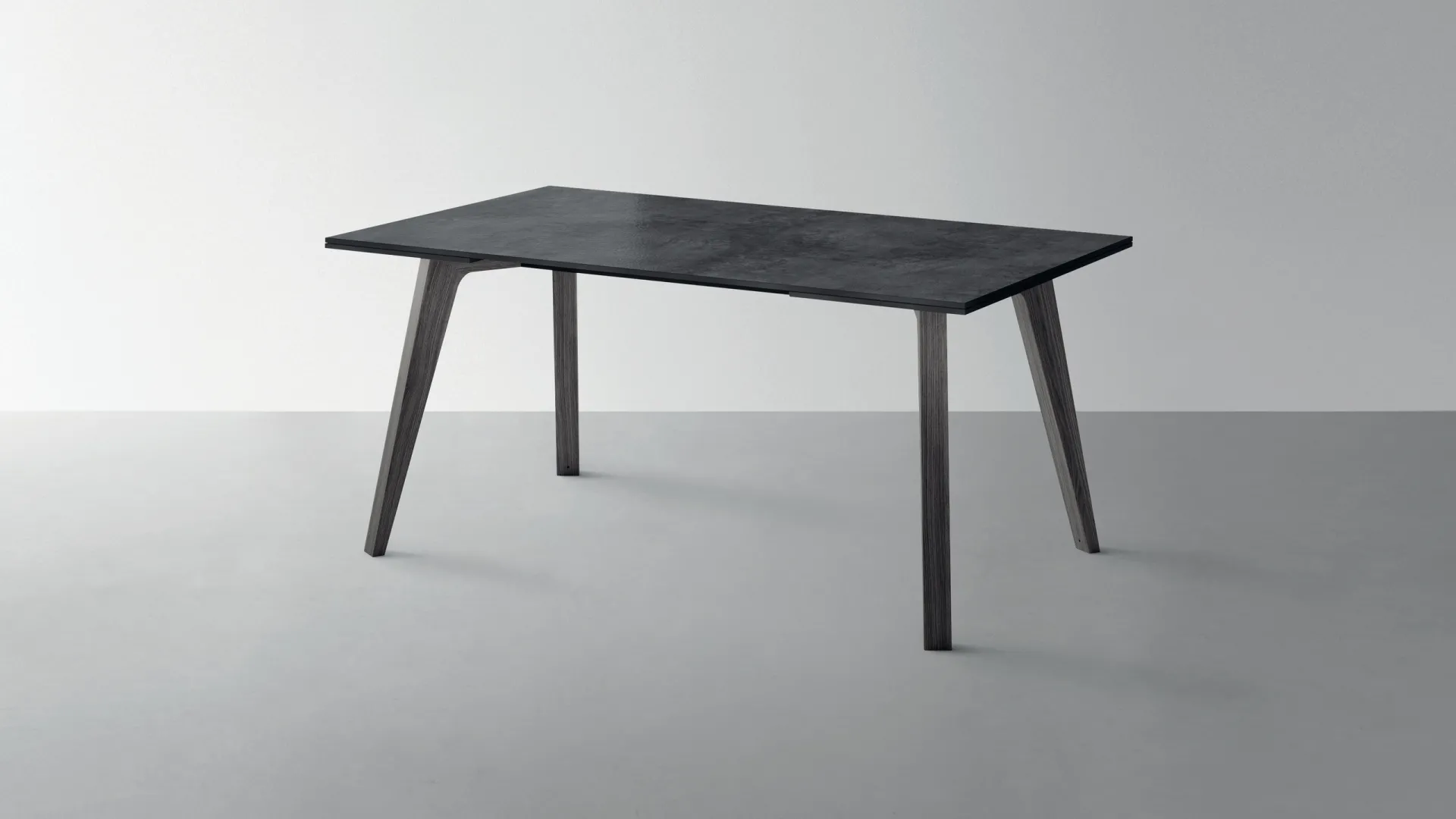 Tavolo Motus Scavolini con piano antracite e gambe divaricate su fondo grigio