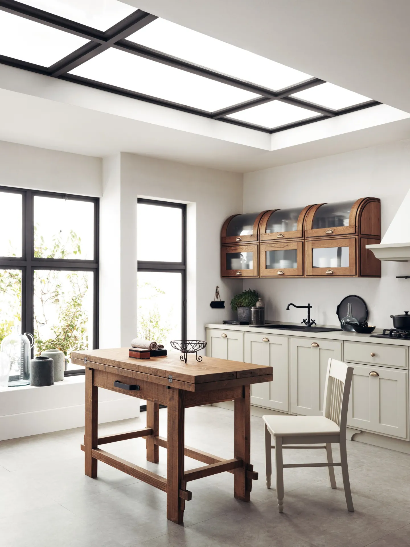 Tavolo Tabula Scavolini in legno con traverse e sedia, davanti a una cucina con vetrine