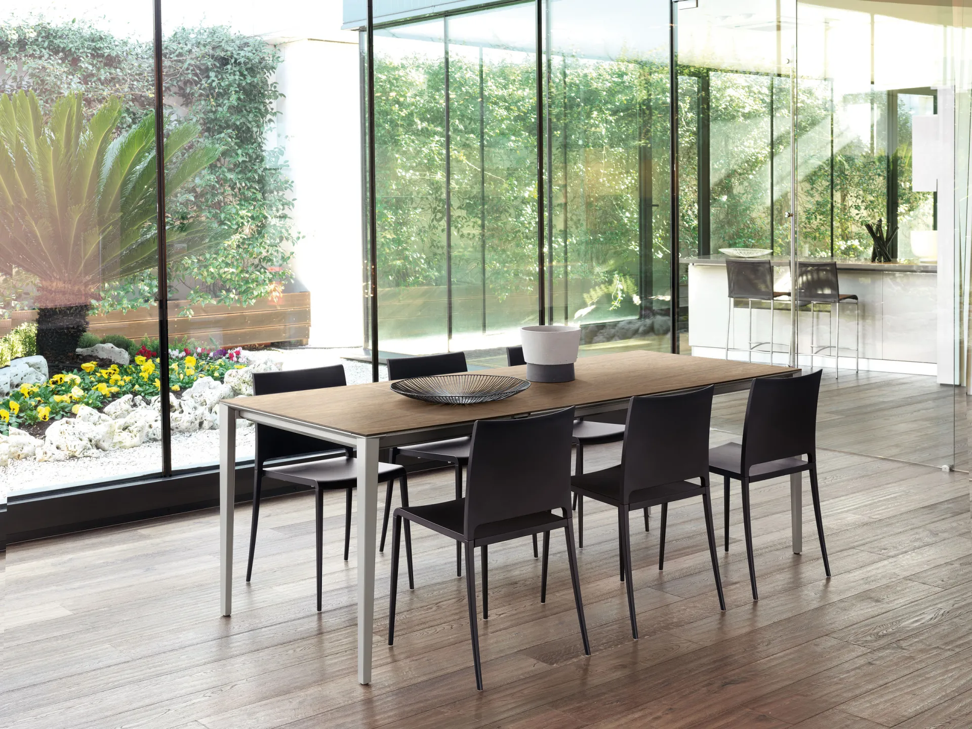 Tavolo Timeless Scavolini allungato con piano effetto legno e sedie nere in una veranda sul giardino