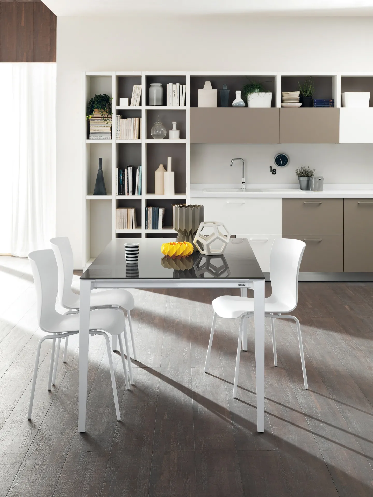 Tavolo Timeless Scavolini con piano scuro e sedie bianche davanti a una cucina con libreria