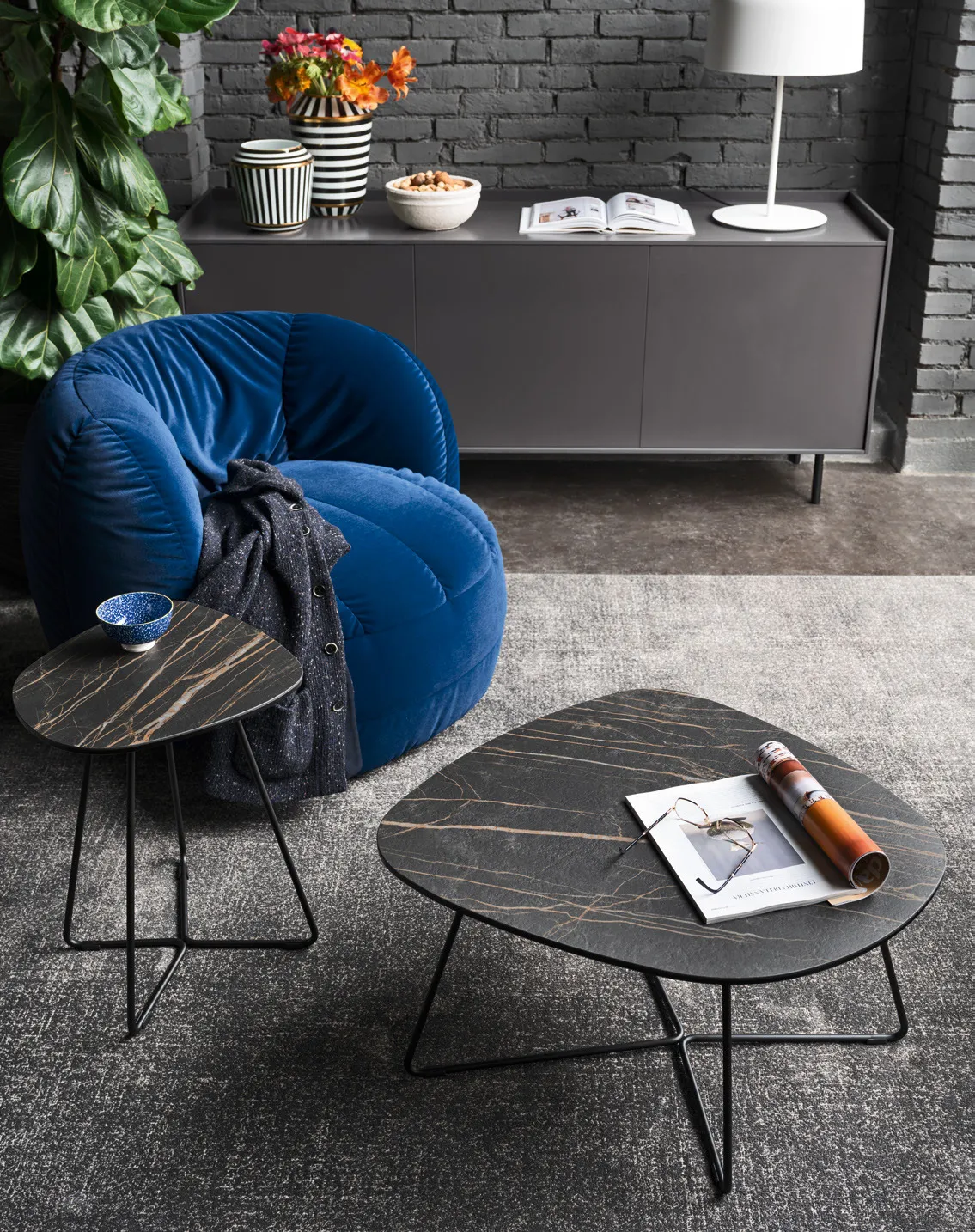 Due tavolini Ciop Connubia con piano in ceramica nera e base nera accanto a una poltrona blu