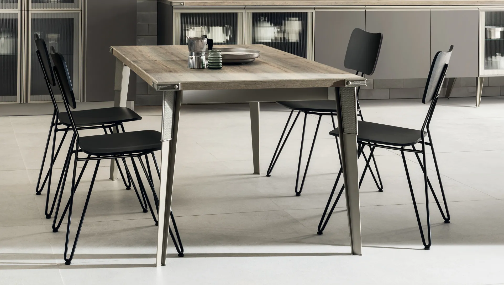 Open Workshop Table Scavolini con piano effetto legno grigio, gambe in acciaio inclinate e sedie nere in filo