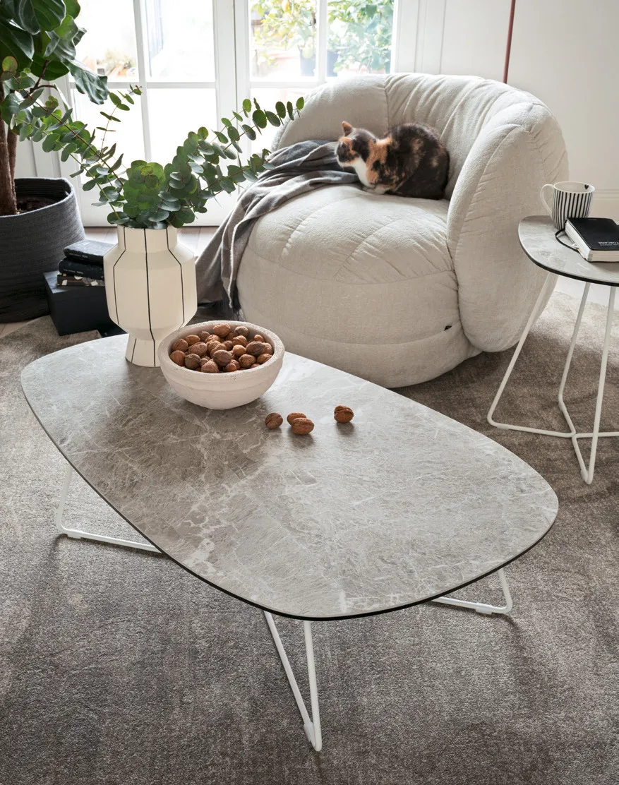 Tavolino Ciop Connubia grande con piano in ceramica arenaria e base bianca davanti a una poltrona chiara