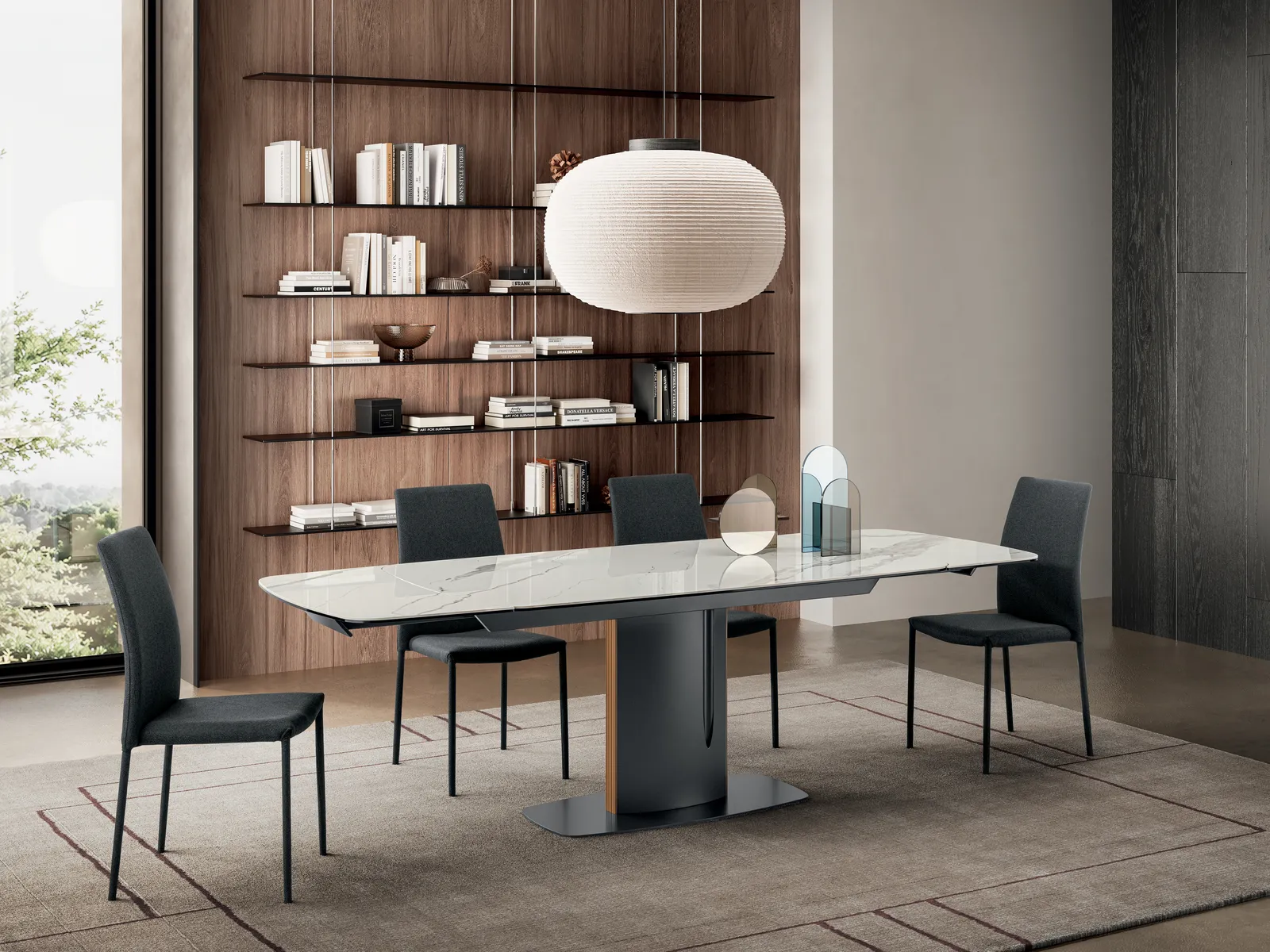 Tavolo Keel Stones in marmo bianco lucido con base antracite, aperto davanti a una libreria