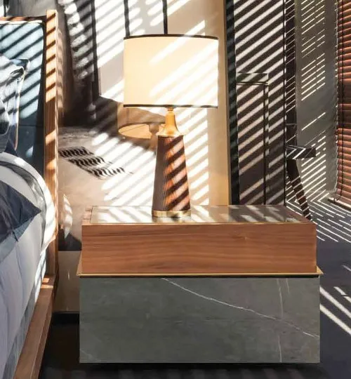 Comodino Della Loggia Bernazzoli in noce canaletto e gres grigio accanto al letto, con lampada