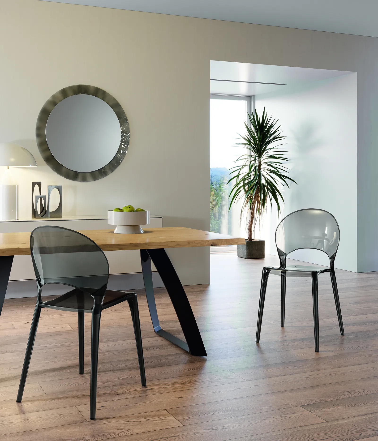 Sedie Pearl Stones in policarbonato grigio intorno a un tavolo in legno, in una sala con specchio rotondo