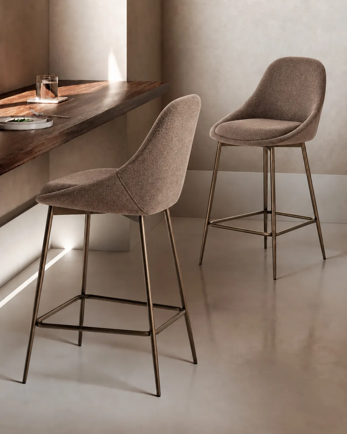 Due sgabelli Kira Stones in tessuto marrone con gambe bronzo accanto a un bancone in legno