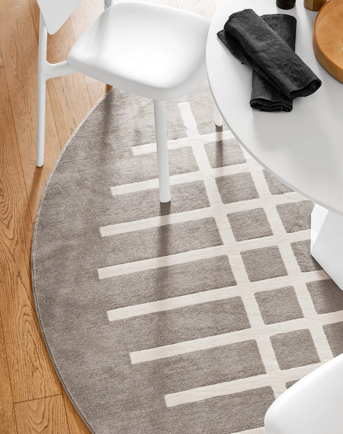 Tappeto Cek Connubia tondo con griglia bianca su fondo beige sotto un tavolo bianco, visto dall'alto
