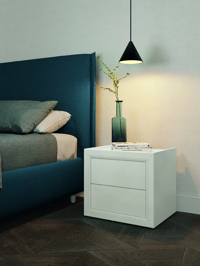 Comodino classico Solid Colombini bianco a riquadri accanto a un letto blu petrolio