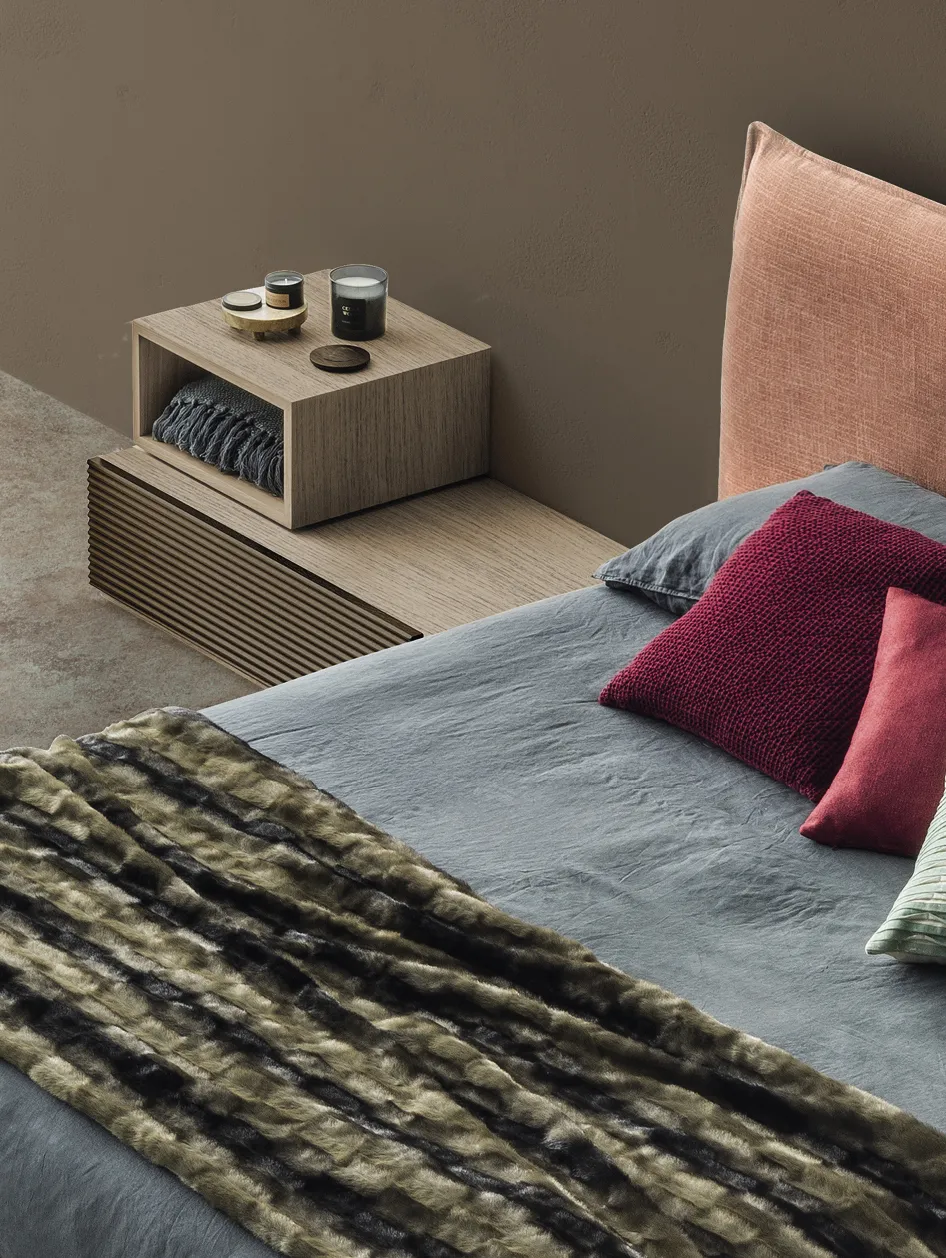 Comodino Brick Devina Nais con vano a giorno accanto a un letto con cuscini colorati