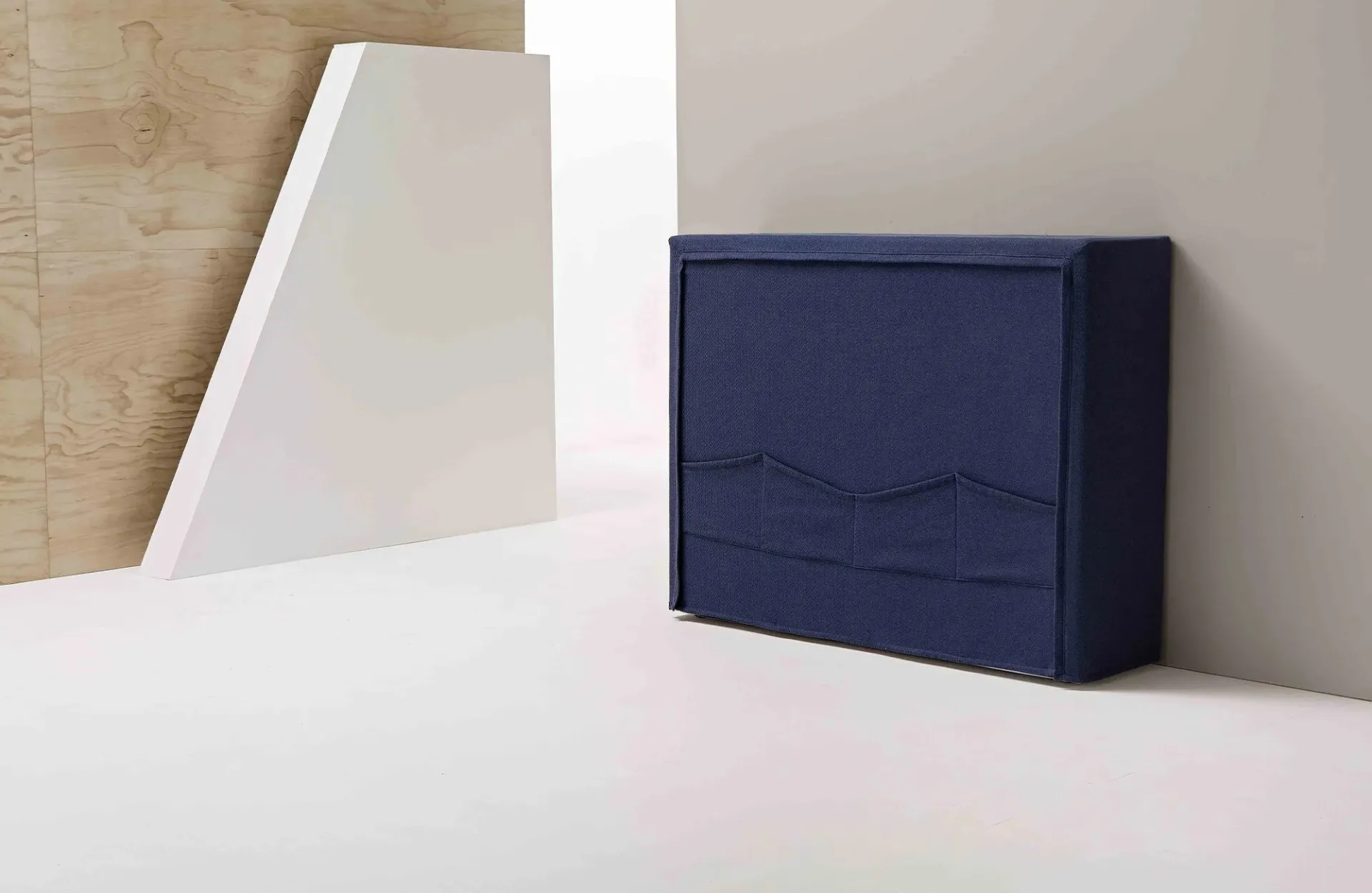 Letto pieghevole Pagetto Dienne chiuso, mobile imbottito blu appoggiato a una parete chiara