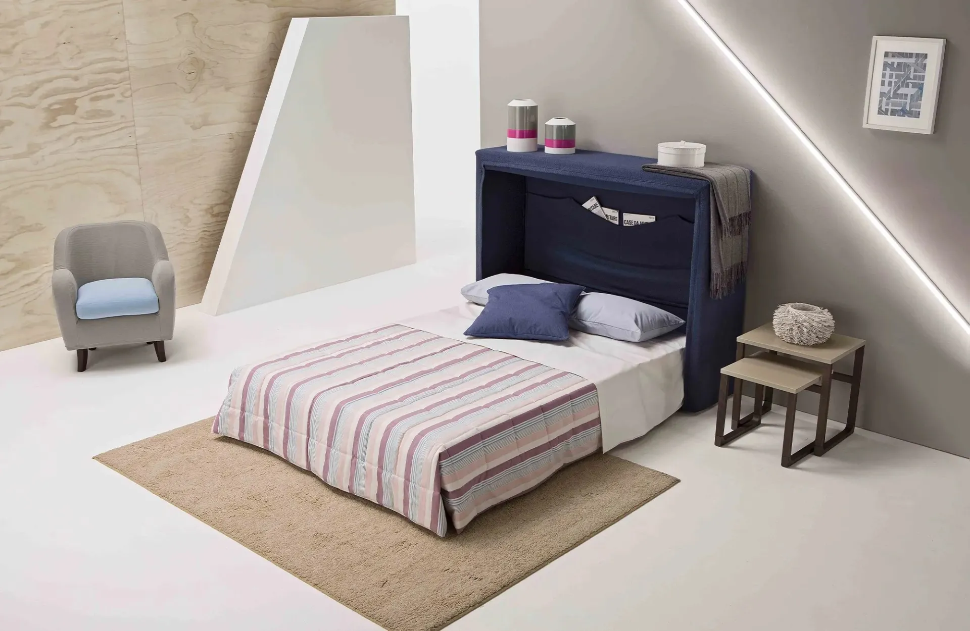 Letto Pagetto Dienne aperto con copriletto a righe accanto a una poltroncina grigia