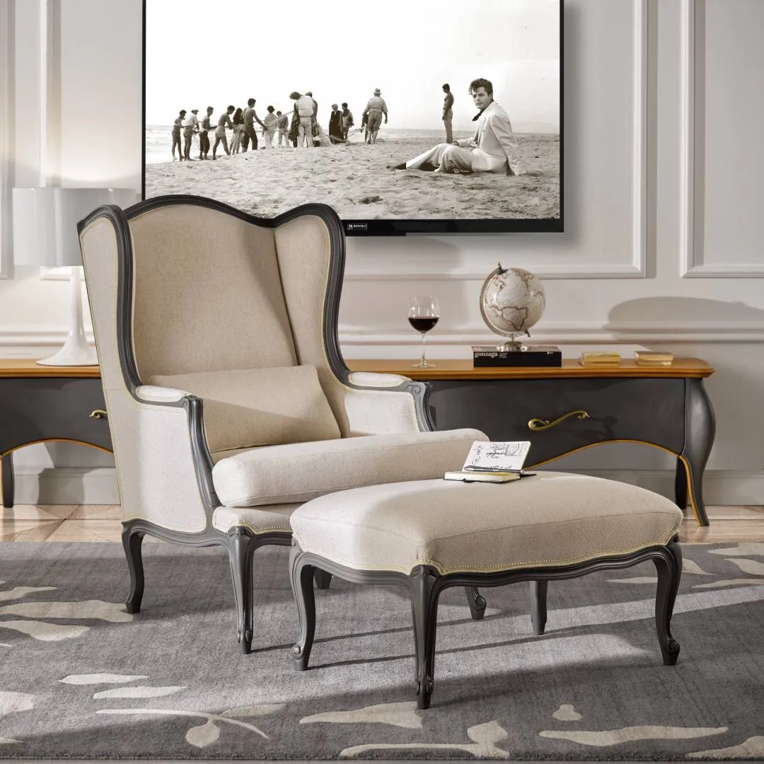 Pouf Tosato 51.07 con gambe curve grigie davanti a una poltrona bergère color lino