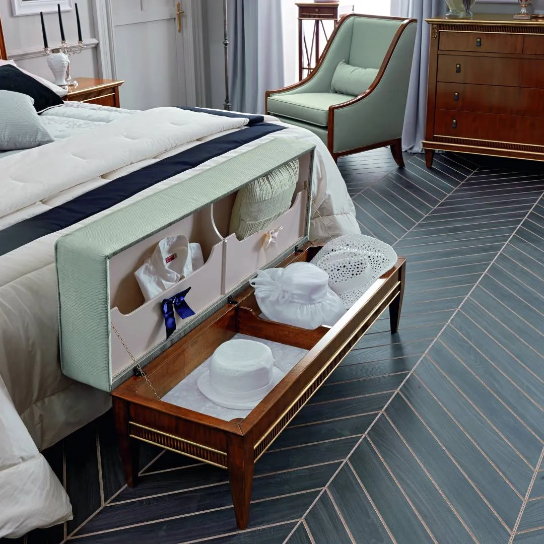 Pouf contenitore Tosato 51.04 aperto ai piedi di un letto, con seduta verde salvia sollevata