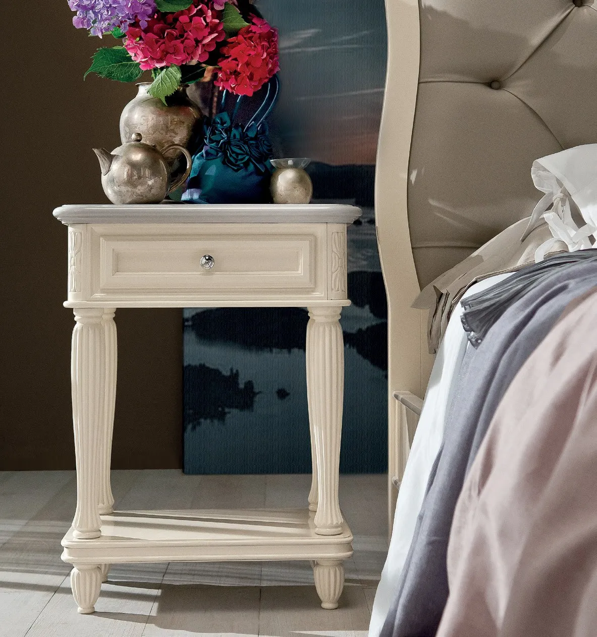 Comodino Marco Polo Imba chiaro con gambe tornite accanto al letto