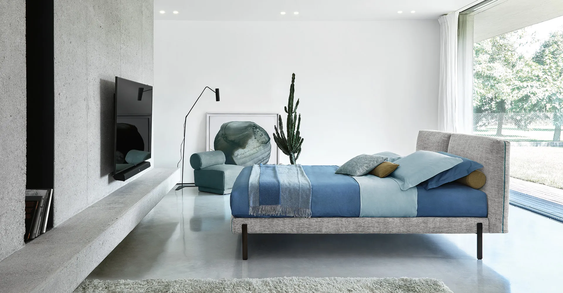 Letto Orione Rosini grigio con lenzuola blu in un soggiorno aperto