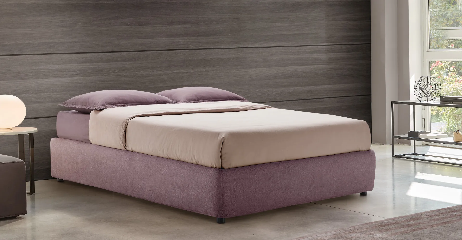Letto Sommier Rosini color malva davanti a una parete scura