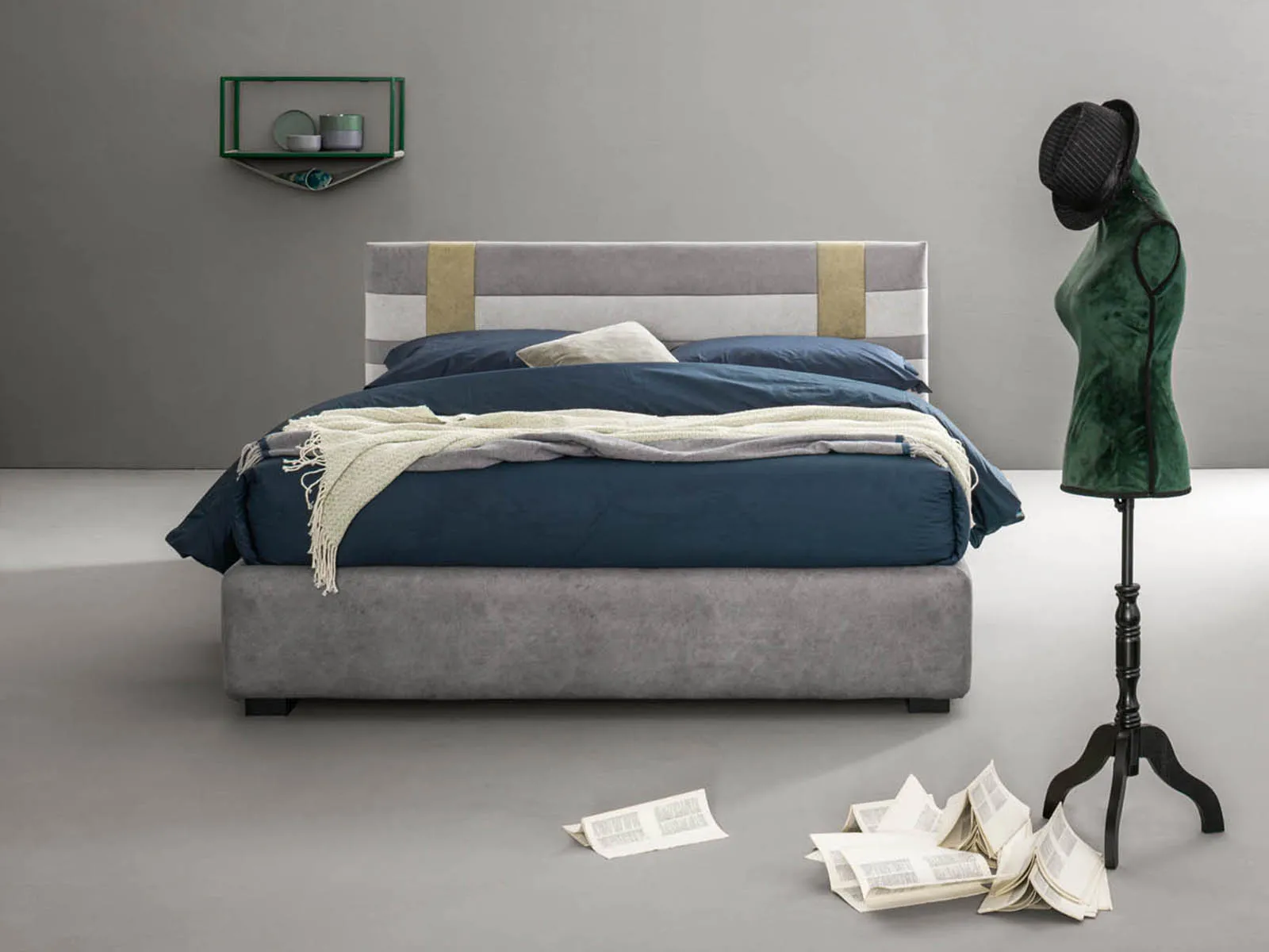 Letto matrimoniale Net Samoa grigio con cinghie color ocra sulla testiera, accanto a un manichino