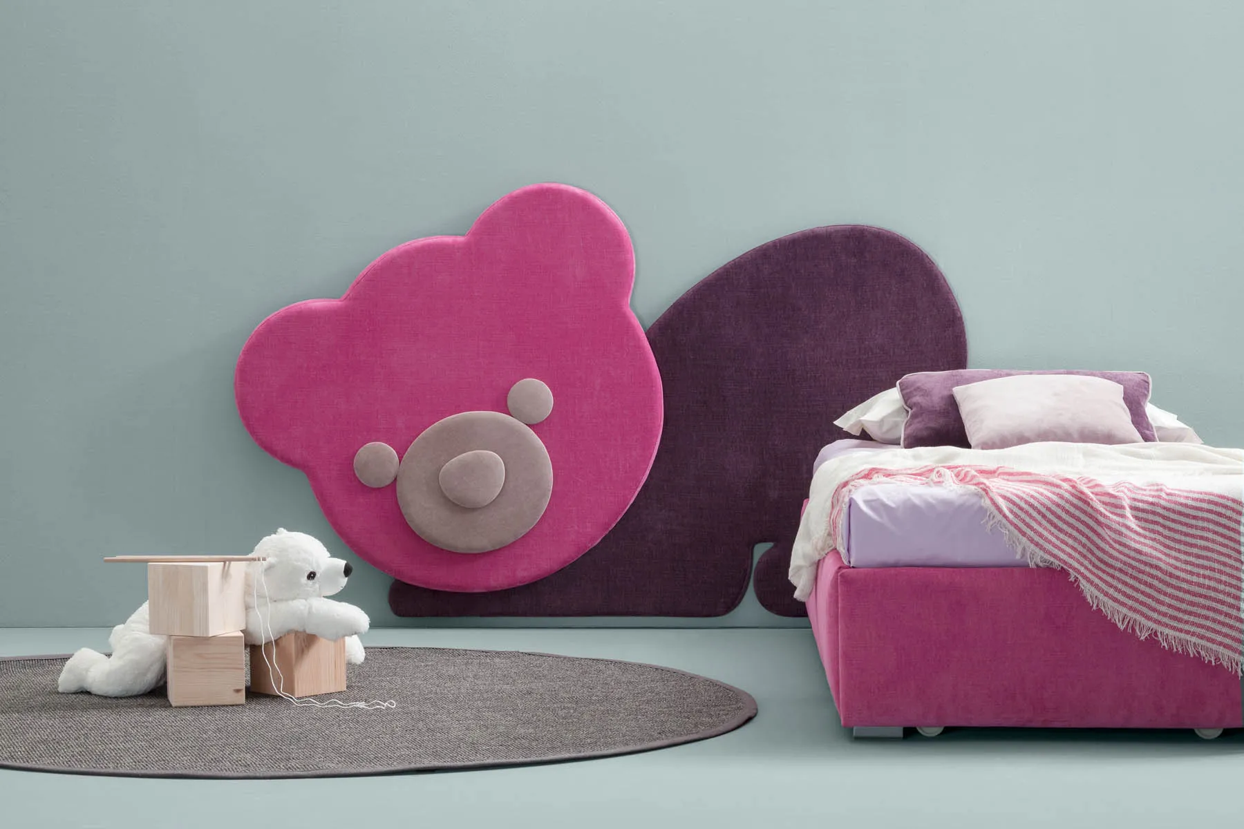 Orsetto fucsia Ted Samoa e sagoma prugna sopra un letto rosa, con peluche bianco