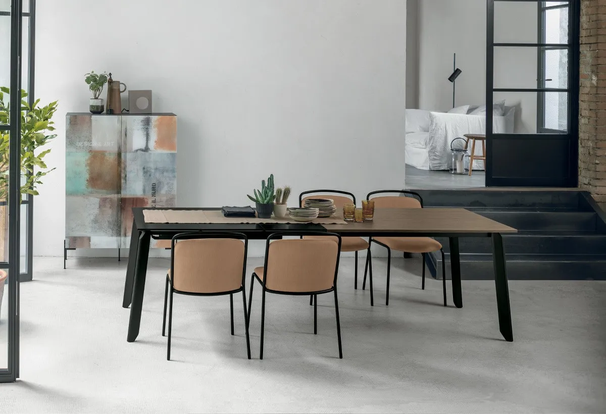 Tavolo Efesto Target Point scuro con sedie color cuoio accanto a una madia decorata