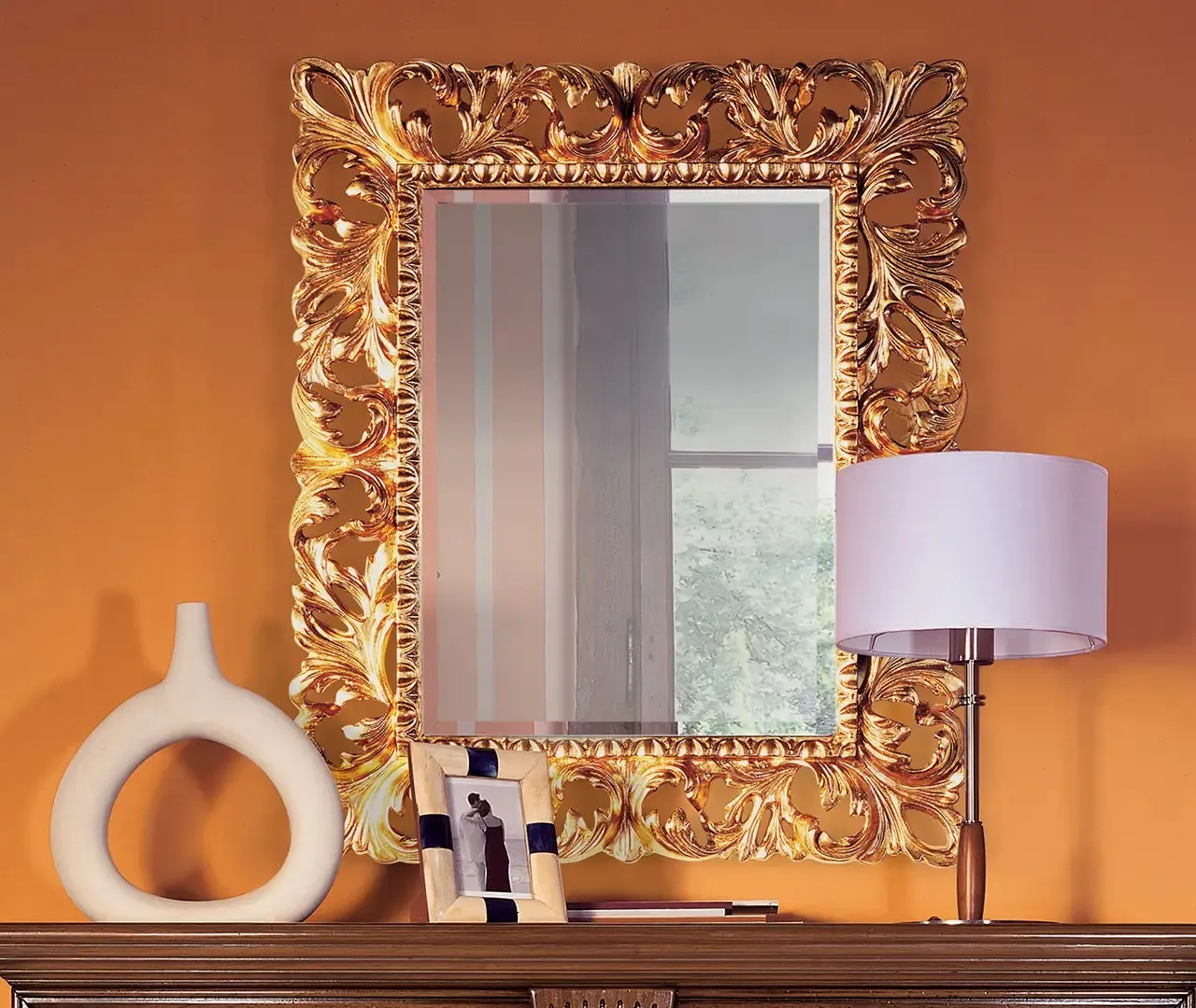 Specchiera classica Bassorilievo Le Fablier con cornice dorata intagliata su parete arancio