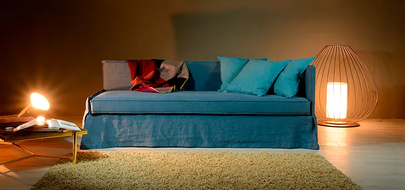 Divano letto Argo Domingo con chaise longue azzurra in una stanza a luce calda