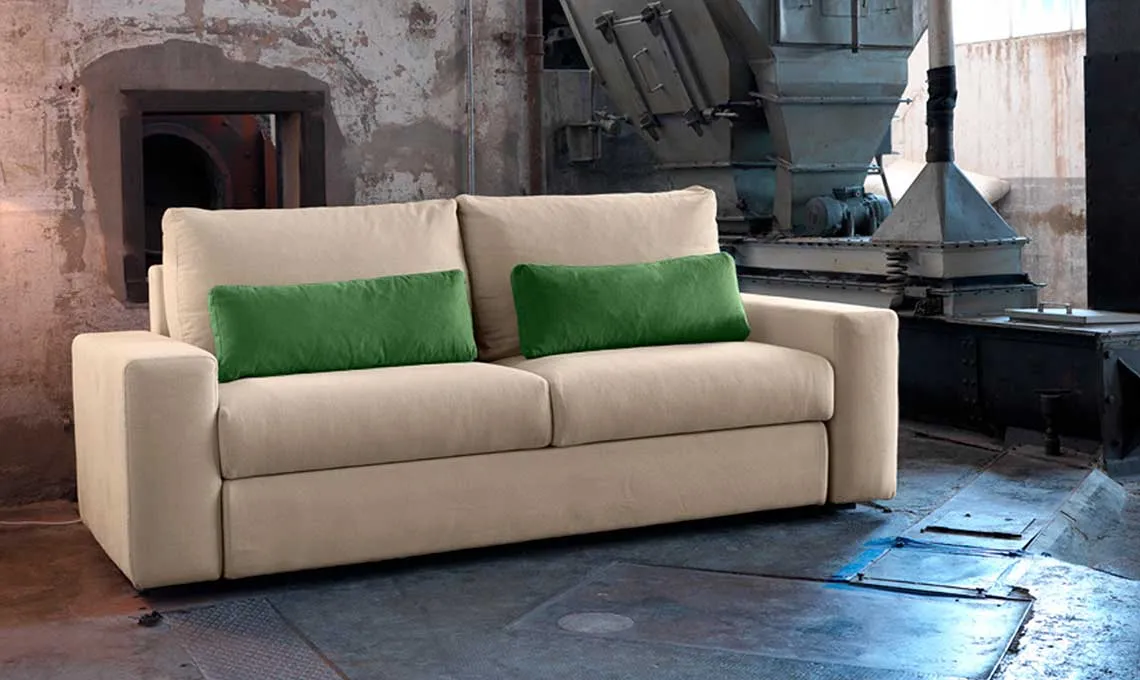 Divano letto Glenn Domingo beige con cuscini verdi in un loft