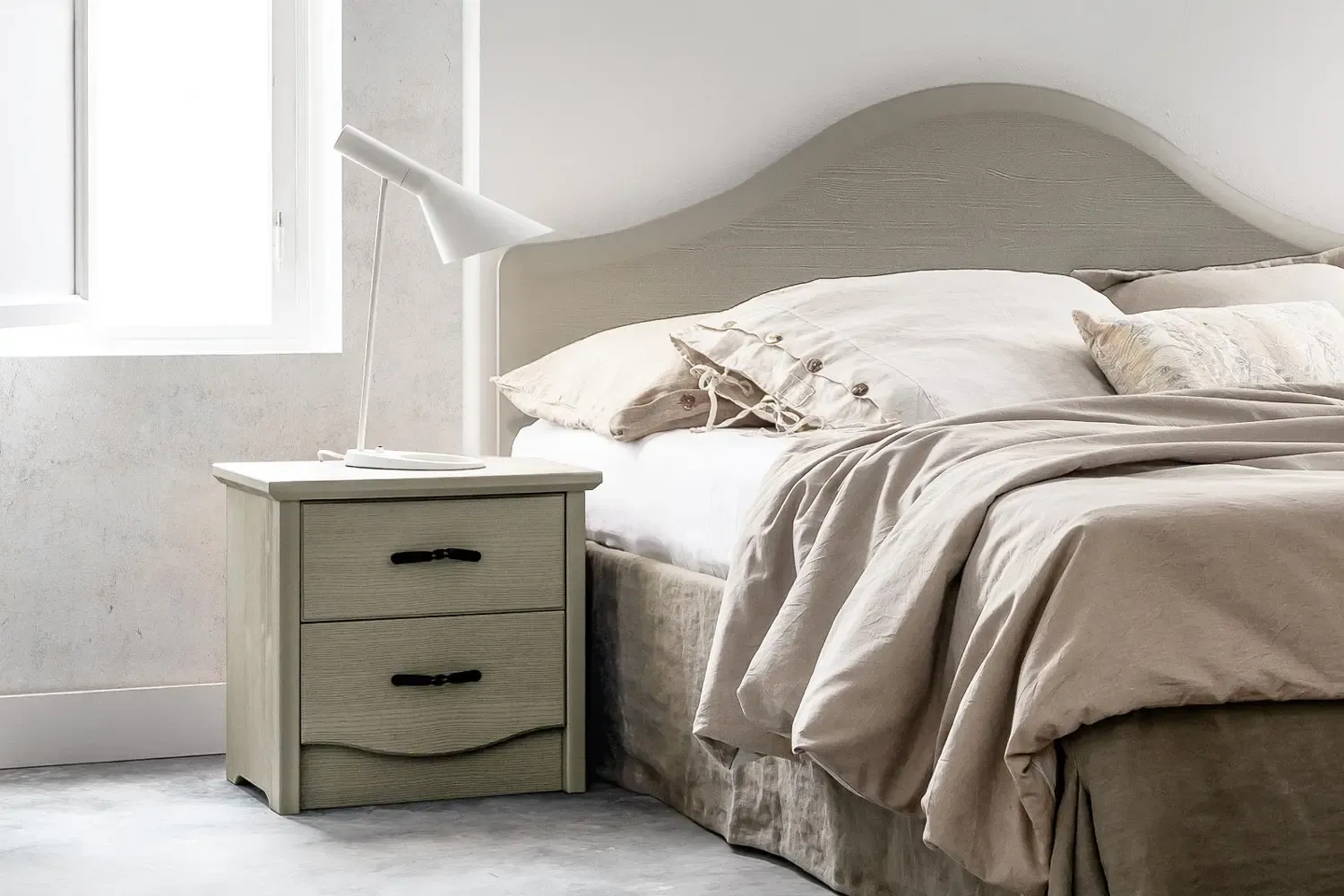 Comodino Eos Callesella grigio verde a due cassetti accanto a un letto con testiera ad arco