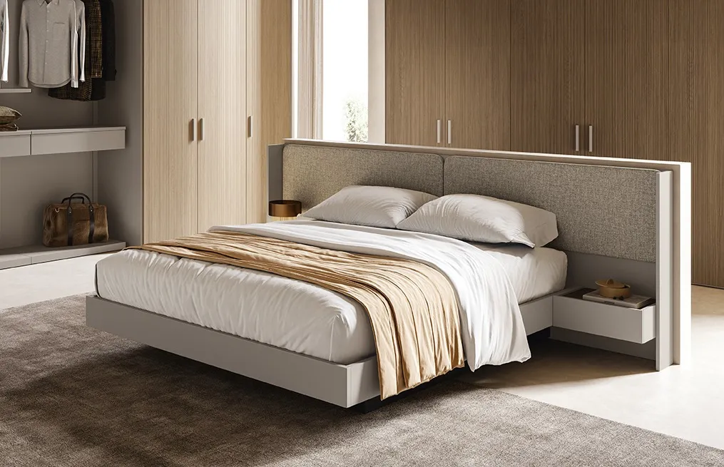 Letto Elios Colombini con cuscini in tessuto beige e telaio tortora davanti a un guardaroba