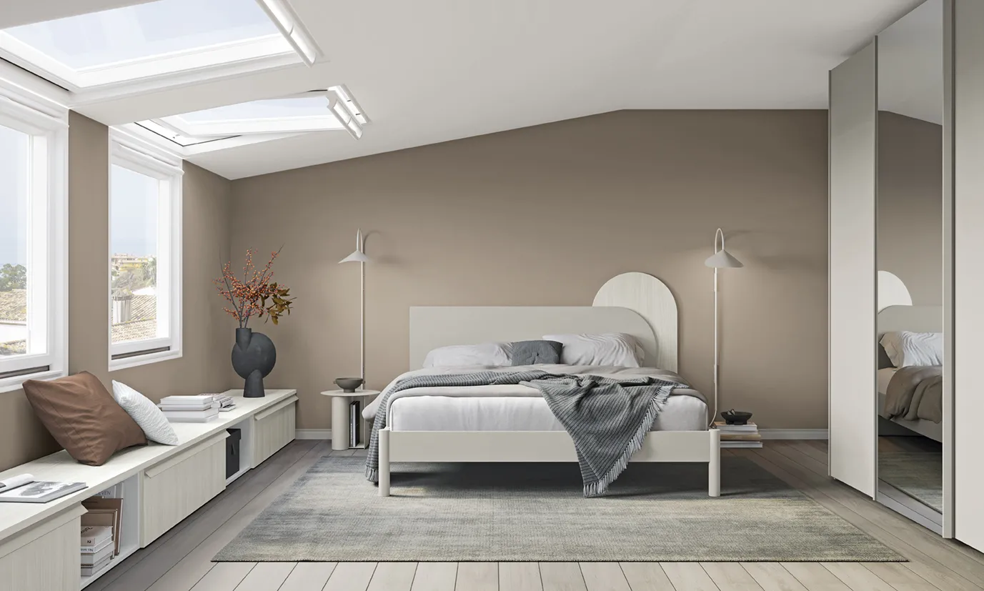 Letto con testata Pill Colombini grigio chiaro con elemento ad arco bianco in una mansarda