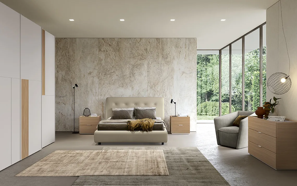 Letto Adagio Colombini color panna davanti a una parete effetto pietra con comò in legno