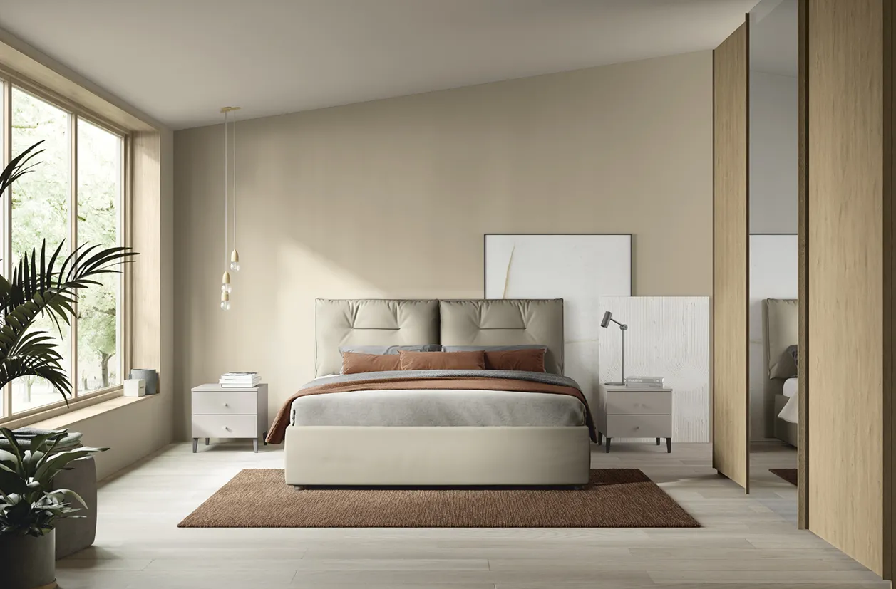 Letto Kiss Colombini color sabbia accanto a una grande finestra con piante