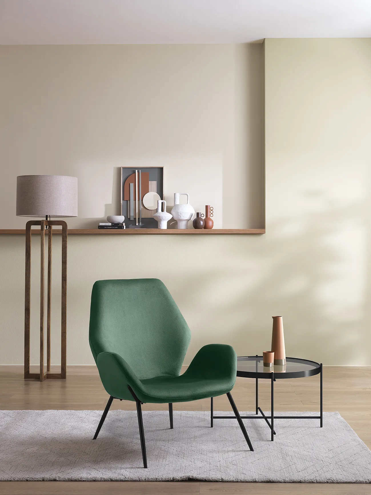 Poltrona Brandy Stones in velluto verde scuro con tavolino rotondo accanto, in un soggiorno luminoso