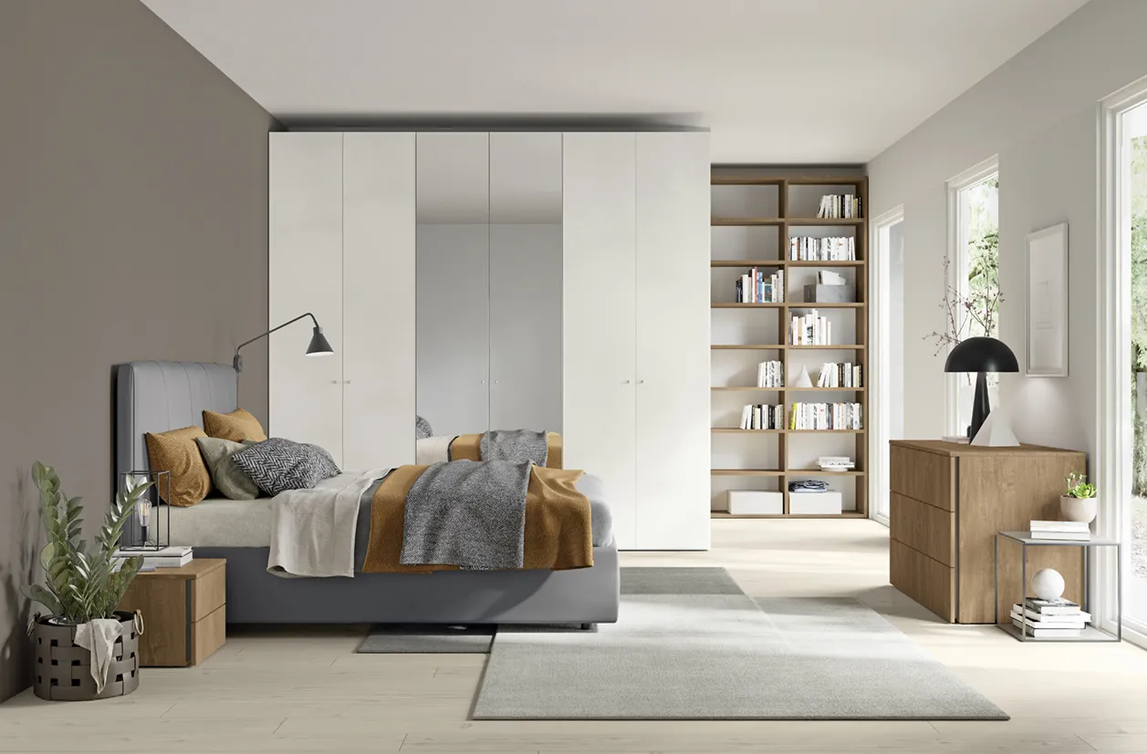 Letto Rapsody Colombini grigio scuro accanto a un armadio bianco e a un comò in legno