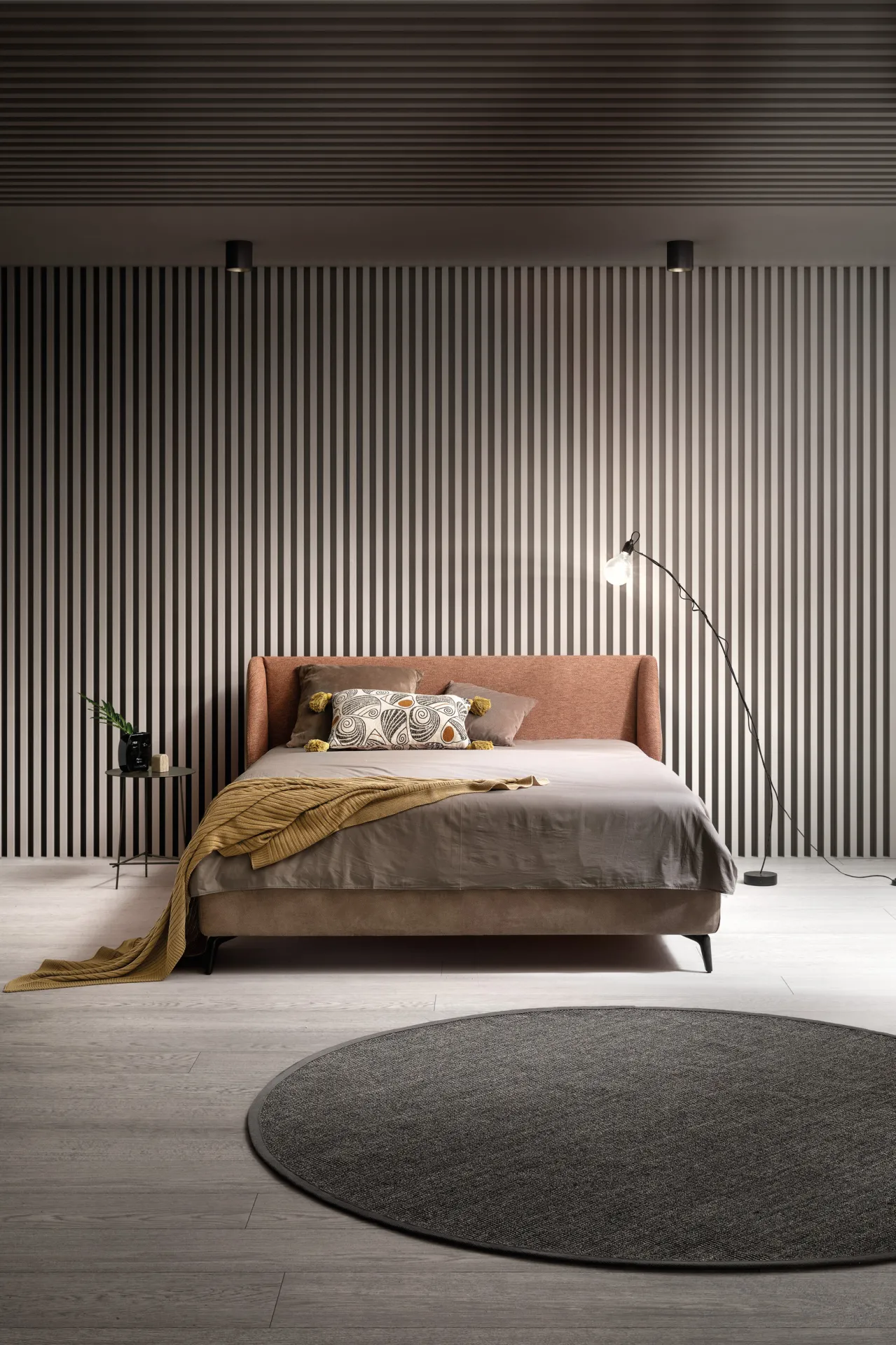 Letto Hug Samoa visto di fronte, con testiera terracotta e coperta senape, su tappeto tondo