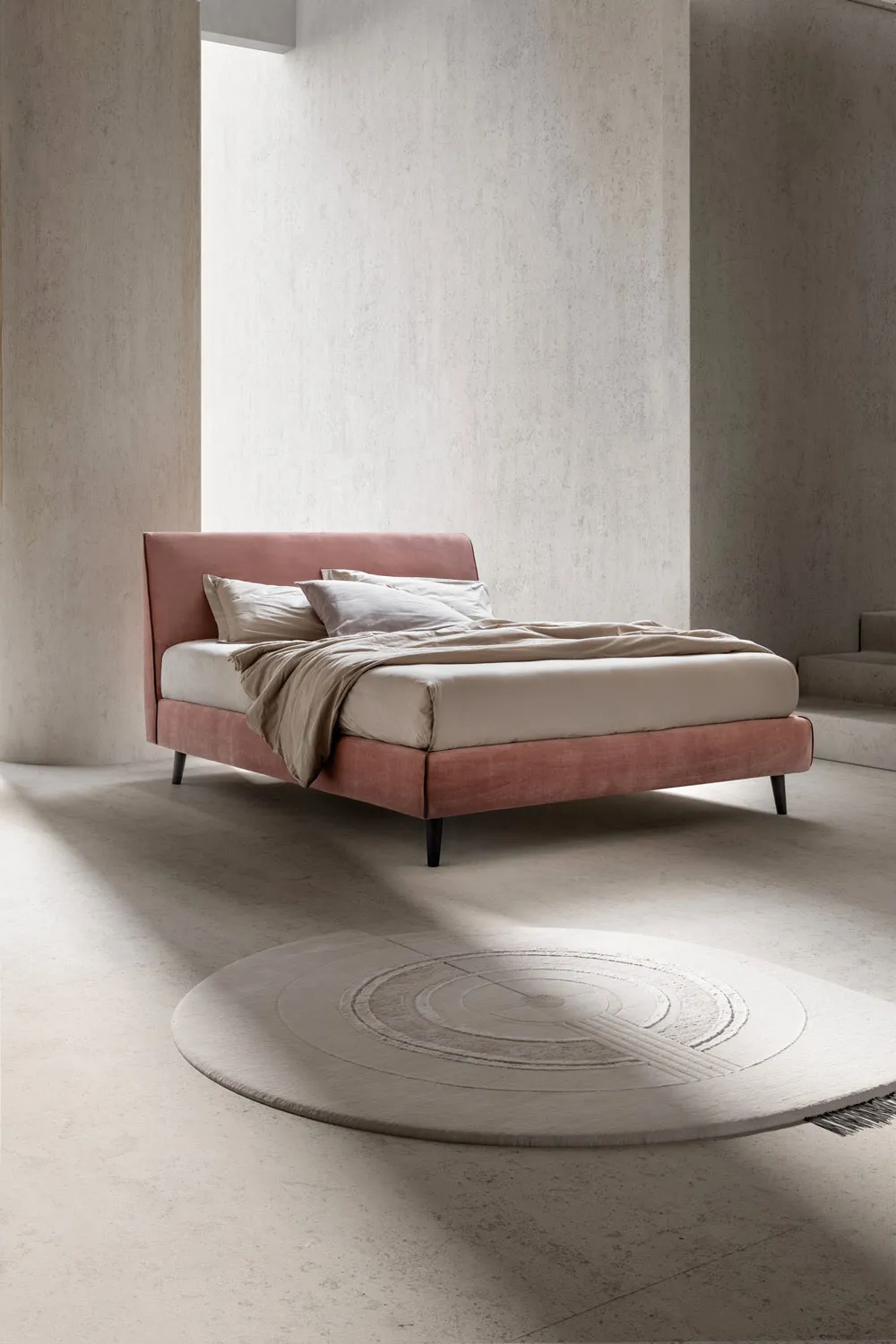 Letto Time Samoa rosa visto di fronte su gambe affusolate scure, con tappeto tondo
